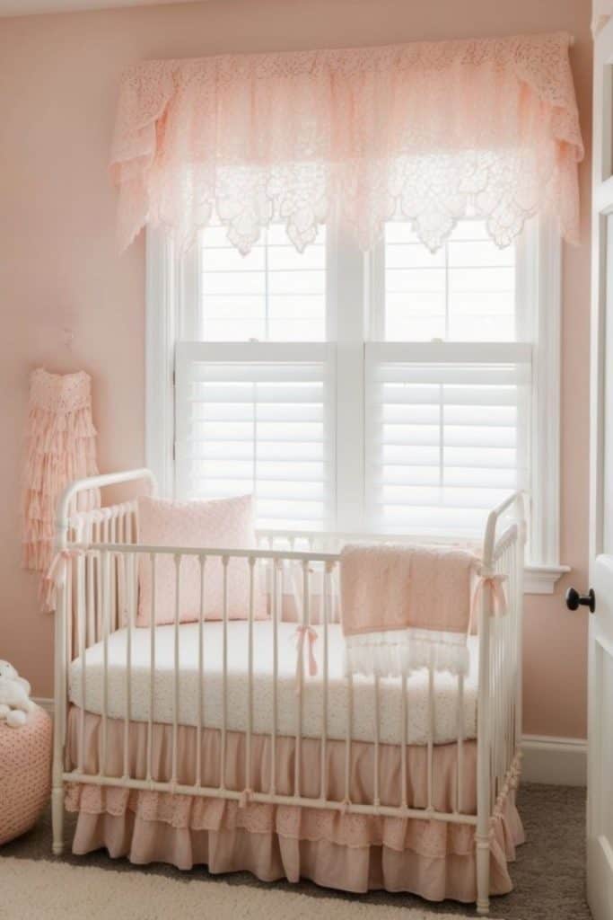 A nursery with a white crib adorned with soft pink bedding and ruffles. The window behind has white shutters and is draped with lacy pink curtains. The walls are painted light pink, and a pink ruffled decoration hangs nearby.
