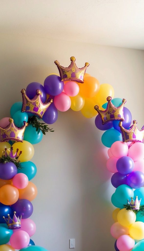 Colorful balloon arch with purple, teal, pink, and yellow balloons, gold crown toppers, and greenery accents.