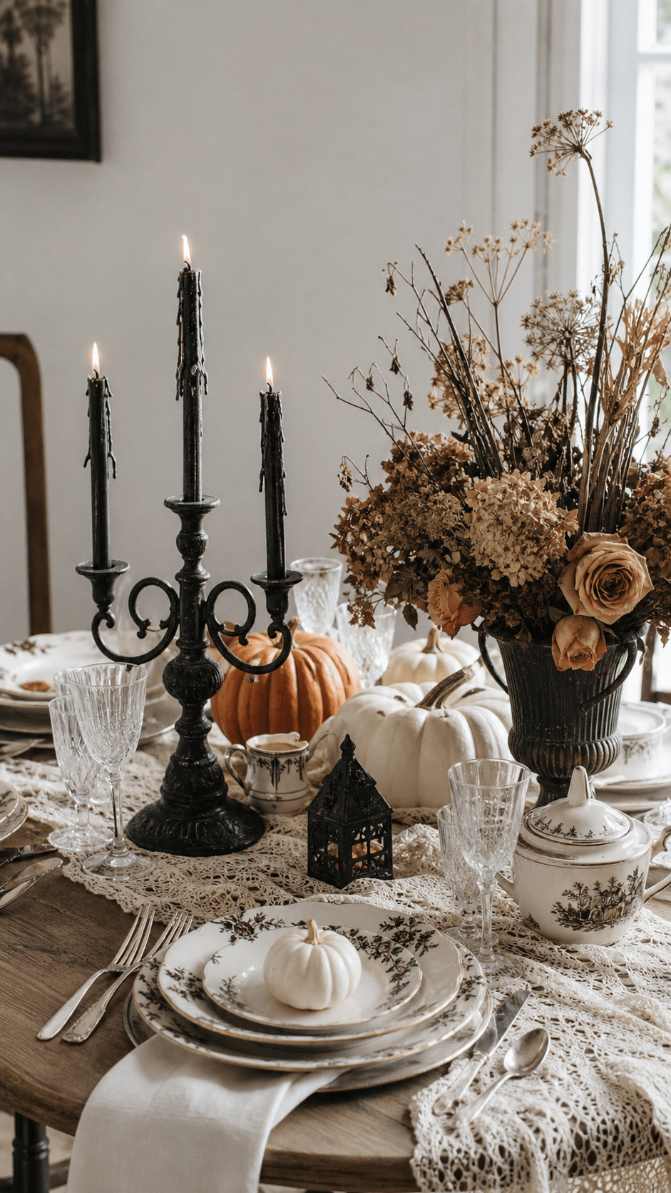Photo of a vintage Halloween tablescape featuring velvet pumpkins in burgundy and moss green, brass candlesticks, scattered amber leaves, and antique plates.