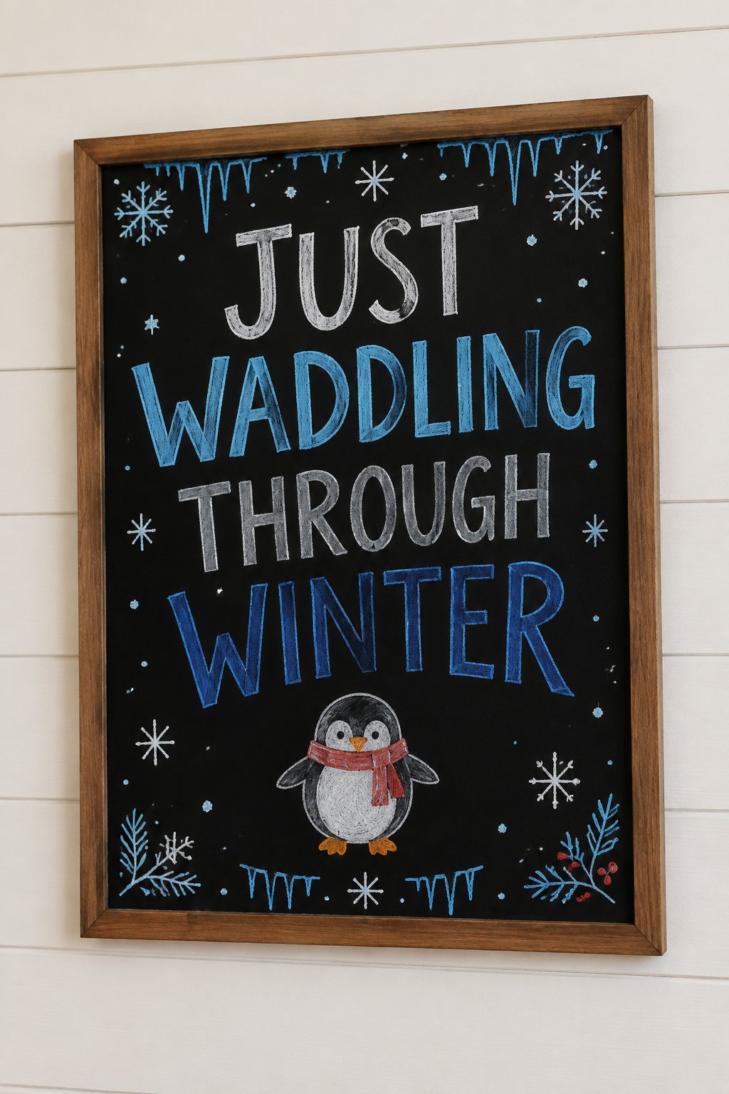 Penguin Waddle Board: a framed winter chalkboard sign reading "Just Waddling Through Winter", hand-drawn in chalk with one round penguin with small flippers and orange feet.